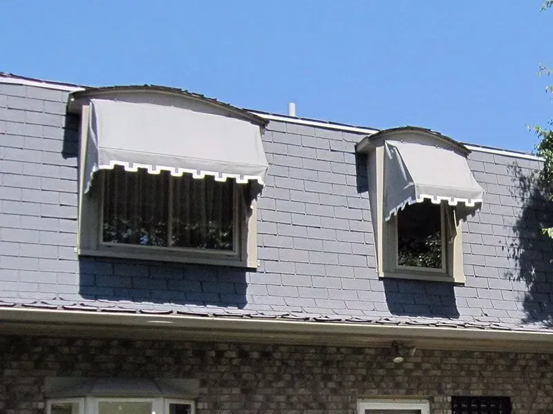 The roof of a house has two windows with awnings on them